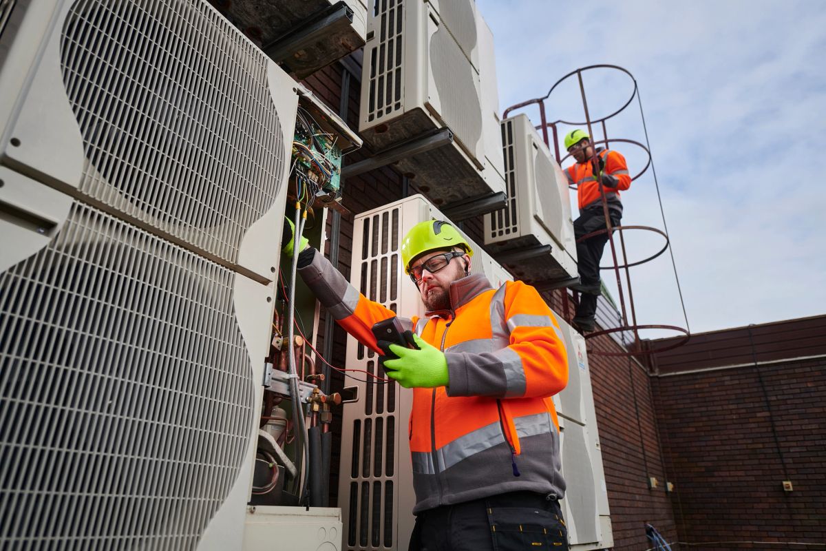 Engineers servicing wall mounted air conditioning condenser units on a commercial building
